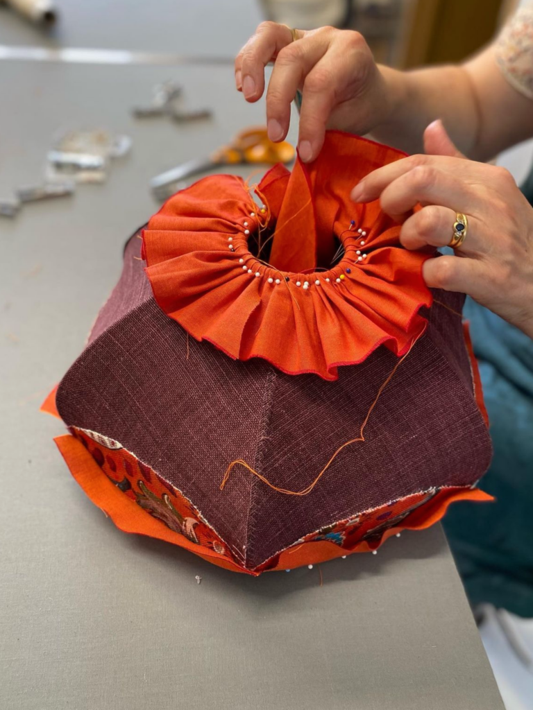 Artisan en train de fabriquer un abat-jour en tissu avec des finitions plissées de couleur orange