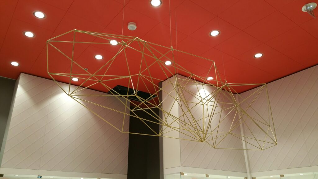 Suspension design en structure métallique dorée aux formes géométriques, installée dans un intérieur moderne