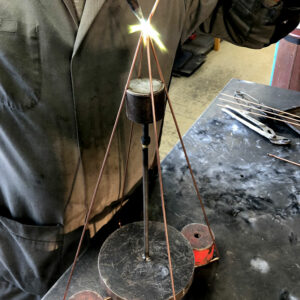 Atelier de soudure où un artisan façonne un cadre de luminaire en métal