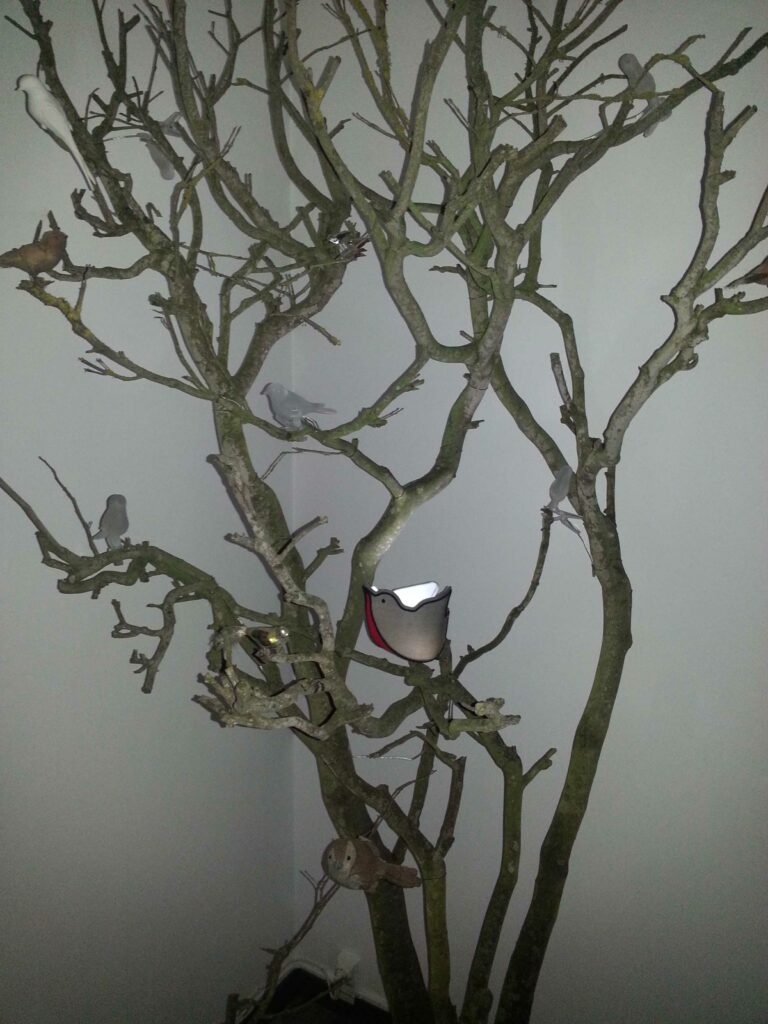Installation artistique d’un arbre avec des oiseaux décoratifs et un luminaire en forme d’oiseau illuminé